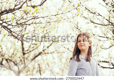 Spring beauty ten years girl with long blonde hair and flowers in her hair outdoors. Blooming trees.