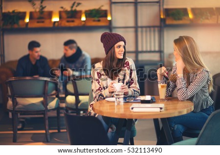 Two friends enjoying coffee together in a coffee shop as they sit at a table chatting