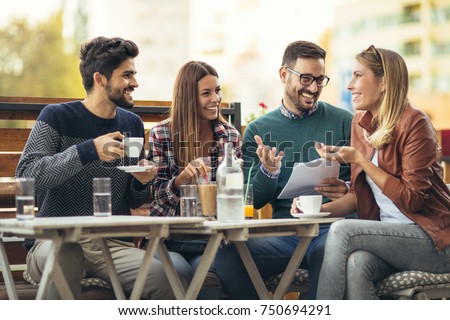 Group of four friends having fun a coffee together. Two women and two men at cafe talking laughing and enjoying their time