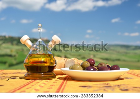 Olive oil, olives and bread on the table against Tuscan landscape. Italy