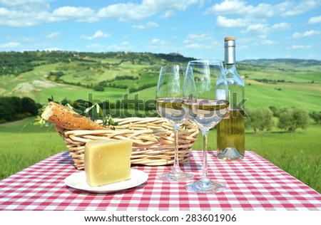 White wine, cheese and bread on the chequered cloth against Tuscan landscape. Italy