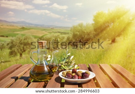 Olive oil and olives and on the wooden table against Tuscan landscape. Italy