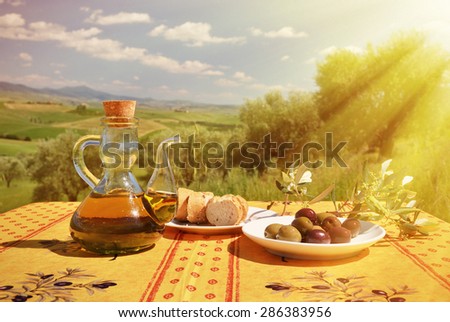 Olive oil, olives and bread on the wooden table against Tuscan landscape. Italy