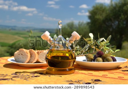Olive oil, olives and bread on the wooden table against Tuscan landscape. Italy