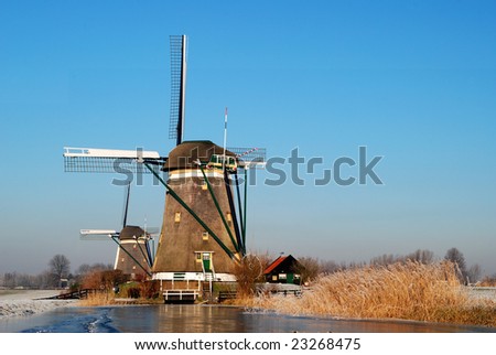 Two windmills in a row with frozen pond