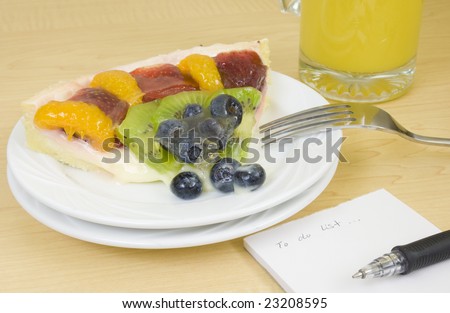 A slice of heavy glazed fruit tart on plate with orange juice, and ready to write a \