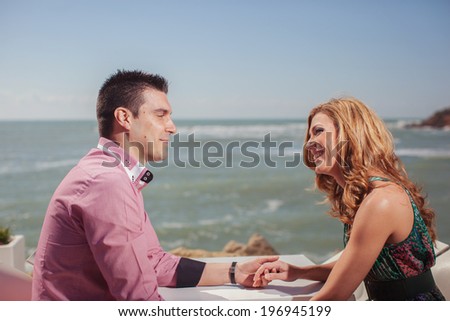 Attractive Young Couple on the Beach. Young couple at the seaside while on their summer vacation sitting at a table on the beach.