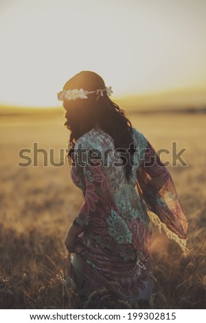 Young woman standing on a wheat field with sunrise on the background
