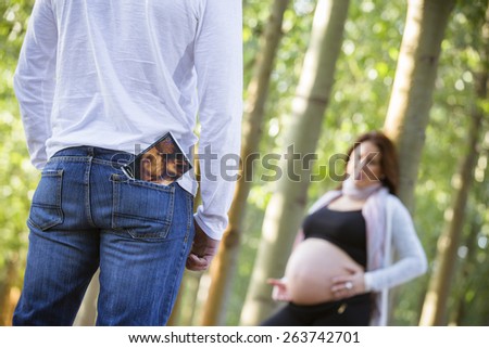 A man stands facing his pregnant woman. Ultrasound picture of baby in his pocket. She is standing in the background and out of focus.Focus on ultrasound image.