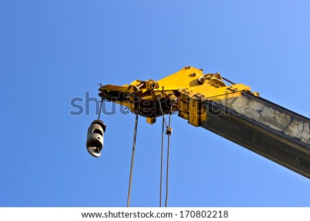 Yellow crane boom with hooks and scale weight above blue sky.