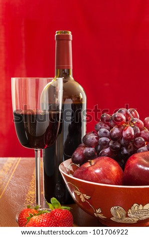 Red wine bottle and red wine in glass with red apples, grapes and strawberries