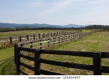 Green pasture land with wooden fences and hills in background