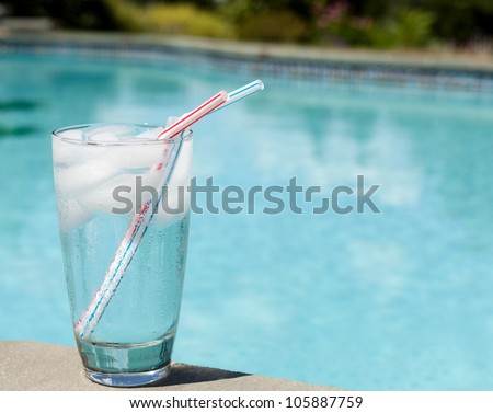 Plain glass of water with ice cubes on side of blue swimming pool