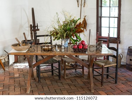 Old fashioned colonial kitchen table chairs food and apples in white room