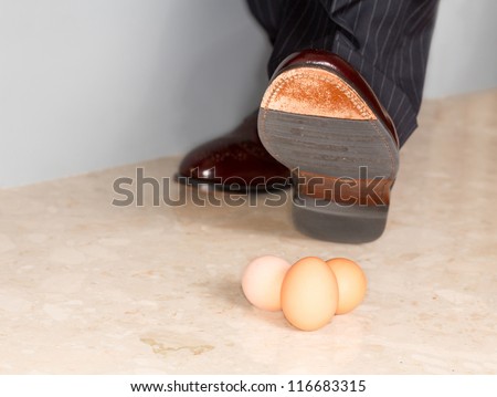 Male brown leather shoe in suit pants about to tread on three brown eggs