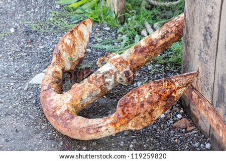 Large metal rusty anchor and rope by side of road on harbor