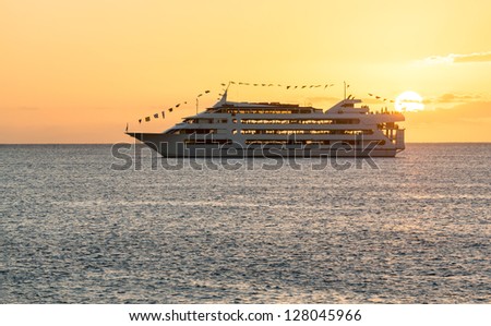 Cruise ship or ferry boat sailing towards setting sun off coast of Waikiki Oahu Hawaii