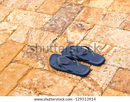 Discarded childs blue flip flops on paved deck by swimming pool with water in indentations