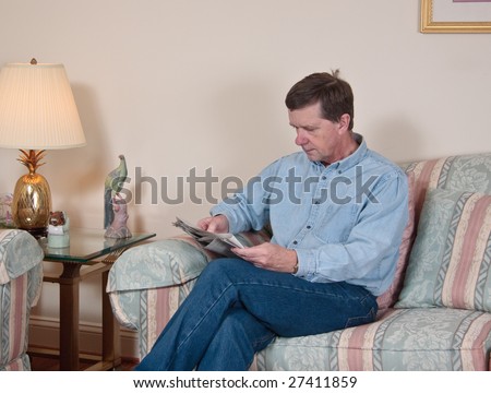 Middle-aged man relaxes on sofa in modern living room reading newspaper