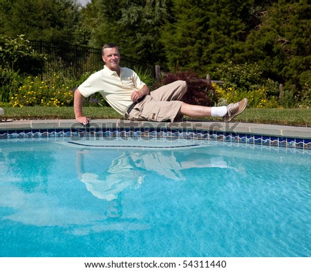 Middle aged man relaxes by the side of a pool in a flowery backyard garden