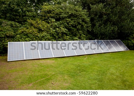 Row of solar panels beside garden hedge facing the sun