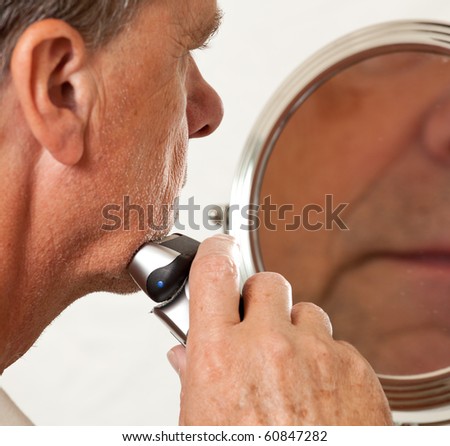 Retired male shaving with electric razor in front of magnifying mirror