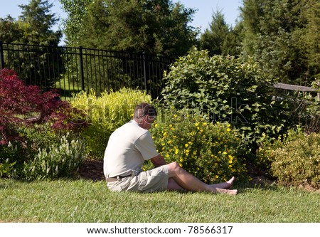 Baby boomer sitting on the grass lawn and digging for weeds in a flowerbed