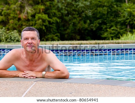 Senior male relaxing by the side of a modern swimming pool in back yard garden and facing the camera with smile