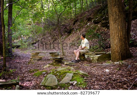 Retired hiker rests on stone benches in a clearing in a forest on a hike