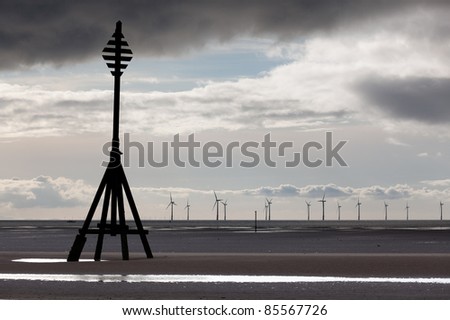 Wind turbines in the ocean off a sandy beach near Liverpool on a cold and cloudy day