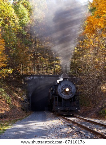 Old steam train pulling out of a tunnel belching steam and smoke