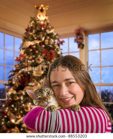 Young bengal kitten held on arm of young woman in front of brightly lit christmas tree