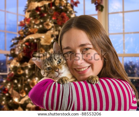 Young bengal kitten held on arm of young woman in front of brightly lit christmas tree