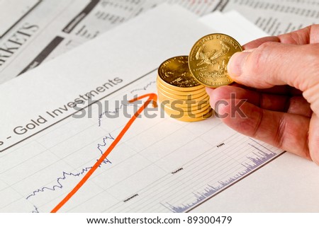 Gold Eagle one ounce coins stacked into graph of gold prices on business pages of newspaper with graphs showing increase in value and hand counting out the money