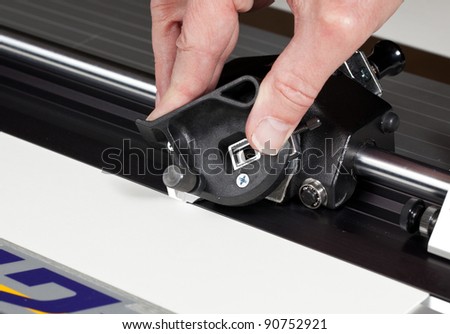 Hand on blade of mat cutter cutting into a white mat for framing a picture