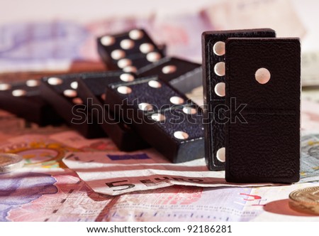 Fallen dominoes with harsh red shadows on pound, euro and dollar bank notes illustrating banking crisis