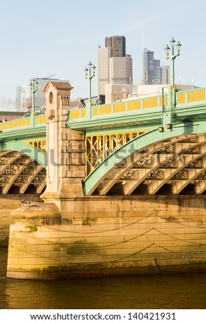 Girders supporting Southwark Bridge across the Thames river in London with setting sun lighting the painted ironwork