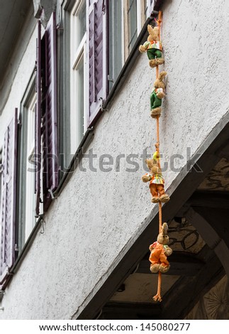 Funny photo of four small stuffed bears and toys climbing down a rope suspended from window of old half-timbered house