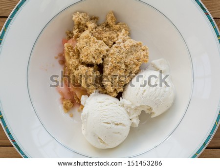 Fresh out of oven in white china bowl apple and strawberry crumble pie in traditional english dessert or pudding with vanilla ice cream scoops