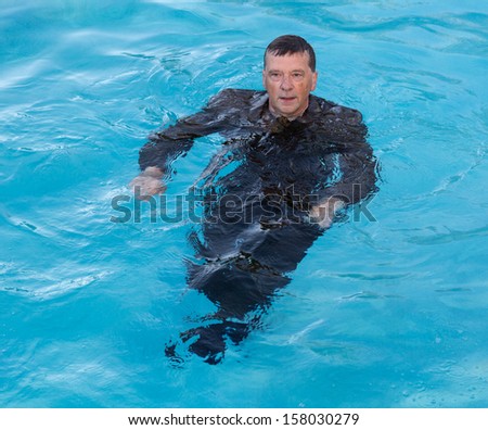 Senior caucasian businessman in suit up to waist in deep blue water and looking worried as he tries to keep afloat