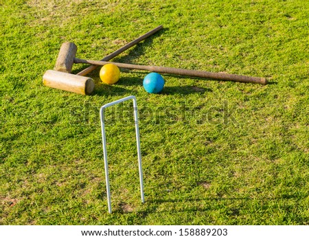 Two wooden mallets of croquet set and hoop set into green english lawn as though the game is just over