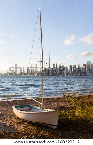 Single sailing boat beached on sandy shore of Lake Ontario on Wade Island of Toronto Islands with skyline of city in the background