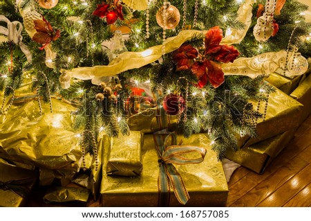 Christmas tree with gold wrapped gifts and presents and lights reflecting off the paper and ribbons under the tree/
