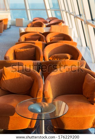 Row of cushioned seats or chairs and towel by high glass window looking out to sea with horizon in the distance