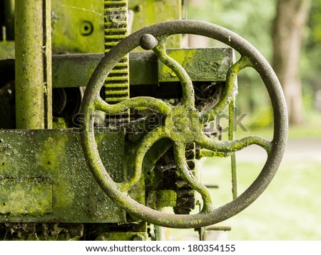 Green lichen covered farm machinery abandoned in forest with turning handle and cogs and gears