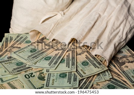 Thousands of US dollars pouring out of a cloth money bag onto a black background showing many currency notes or bills