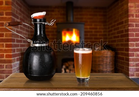 Large 64 fluid ounce four pint growler bottle with a glass of cold beer or ale in front of fire. Used by microbreweries to serve beer for home consumption