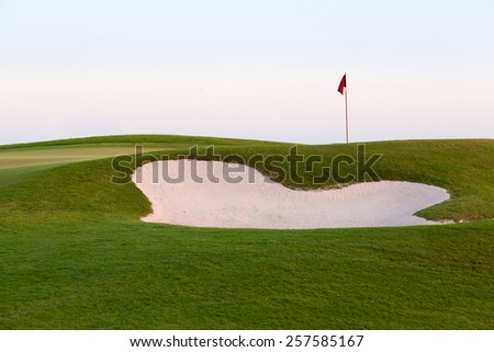 Red flag of golf hole above sand trap or bunker on beautiful course at sunset