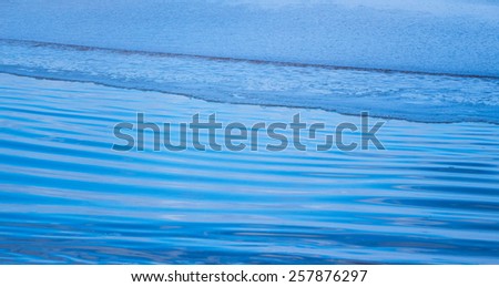Very smooth and calm waves over sand reflecting the blue sky in peaceful seascape scene