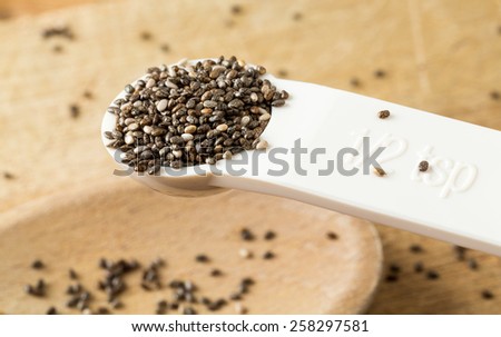 Superfood known as black chia seeds in white plastic measuring spoon over wood bread board on kitchen table